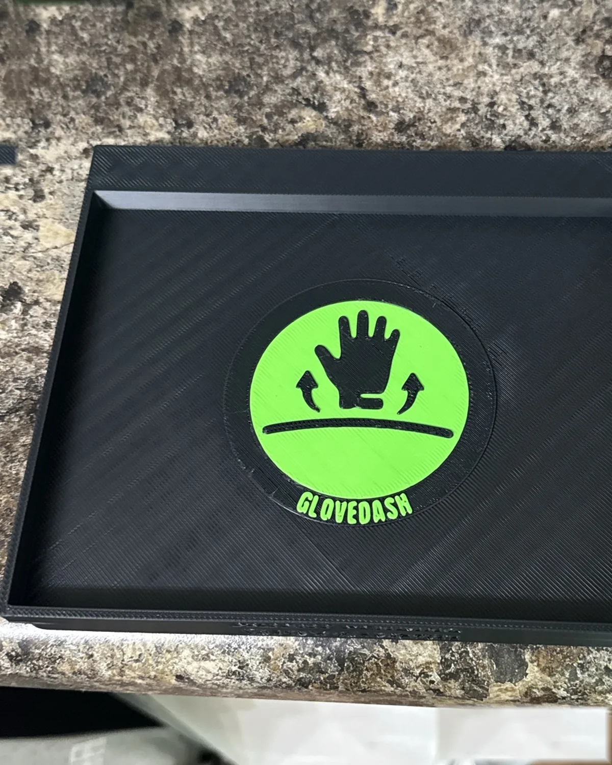 Looking down at a black GloveDash tray with the safety green logo badge in the center