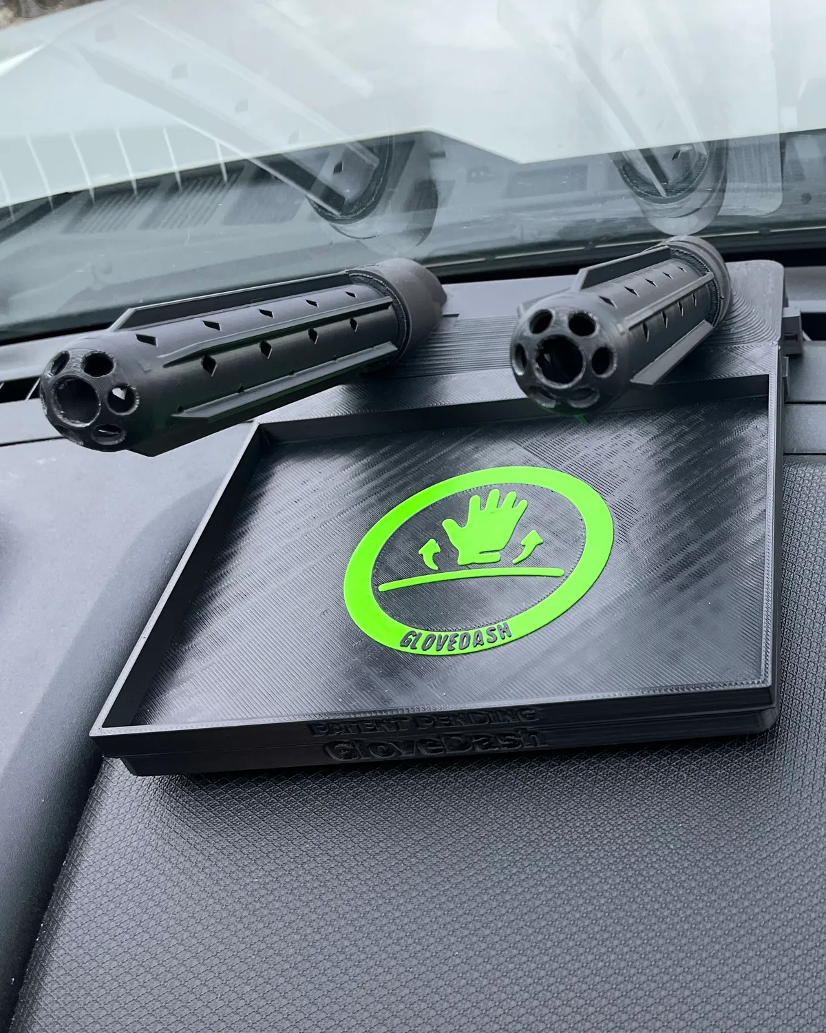 A black GloveDash on a truck dashboard with both tubes twisted off and lying beside the tray, vent holes and open end hubs facing the camera